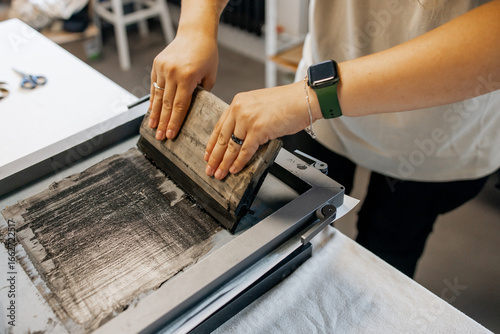 Obraz na plátne Manual Silk Screen Printing on Fabric – Close-up of Hands Working with Screen Pr