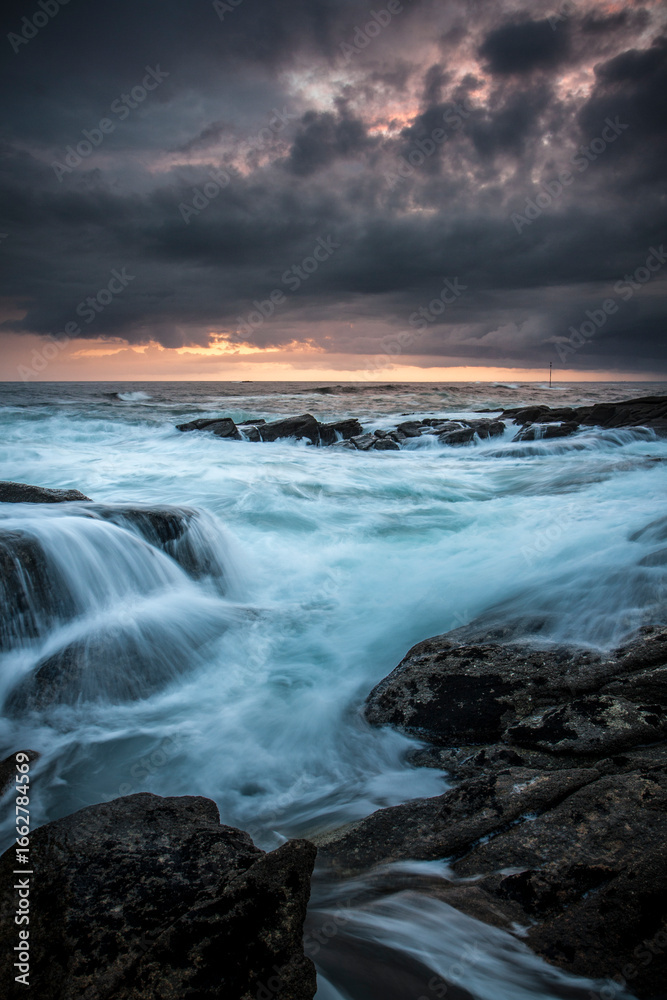 Fototapeta premium Lorient Morbihan Dark storm clouds over powerful waves rushing against rocks.
