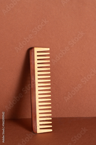 Wooden comb on brown background with shadow for natural hair care, enhances beauty routines with a sustainable touch. Minimalist style