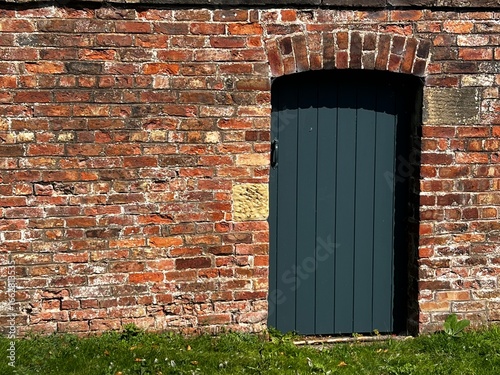 Wooden painted garden gate in a brick wall with green grass in foreground