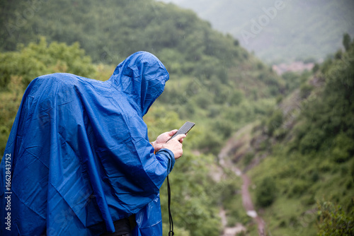 Photos Hiker wearing blue poncho using smartphone in the rain while hiking in the mount