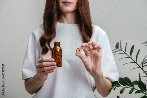 A woman holds omega-3 fish oil capsules. Healthy lifestyle, prevention and treatment of diseases. The woman takes and drinks dietary supplements and vitamins for skin, nails and hair. 