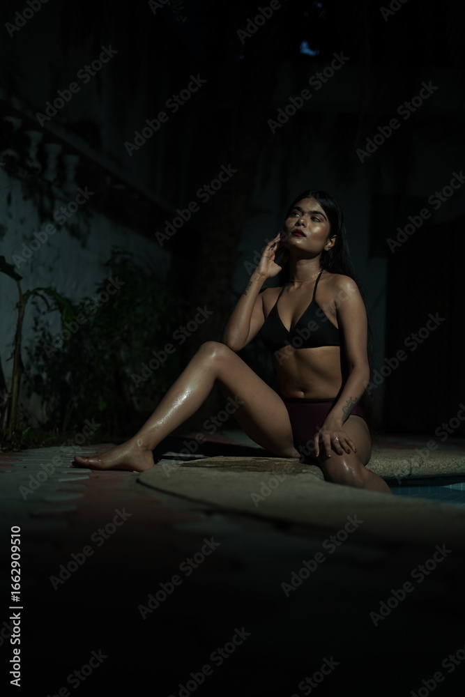 Naklejka premium Woman in Bikini Sitting with One Leg Folded, Poolside Summer Pose