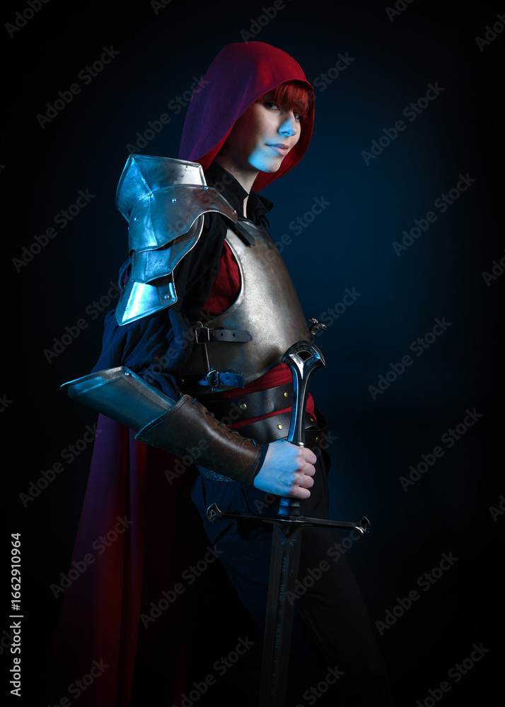 Naklejka premium Fantasy warrior woman with red hair in historical medieval armour costume and red fairytale cloak, cinematic studio portrait of strong heroine knight, epic battle pose, dramatic silhouette figure.