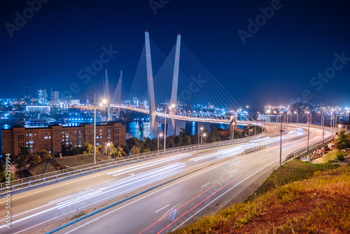 The zolotoy bridge in vladivostok, russia, shines brightly at night, with light trails from cars adding dynamism to the urban landscape