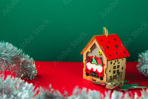 A gingerbread house with a red roof decorated with snow patterns stands on a bright red surface against a dark green gradient background.