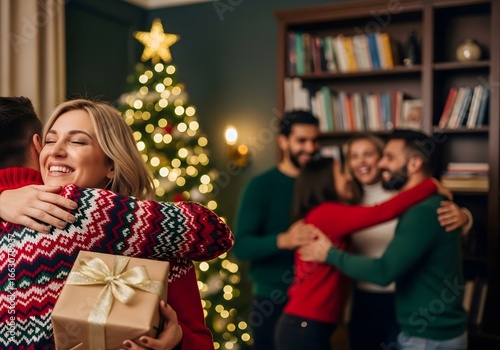 Woman hugs man holding christmas gift with friends and tree in background