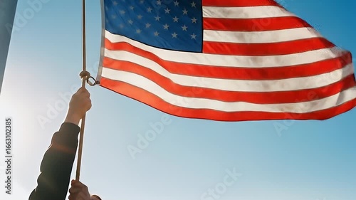 Hand Raising The American Flag Against Blue Sky with Red and White Stripes and Stars