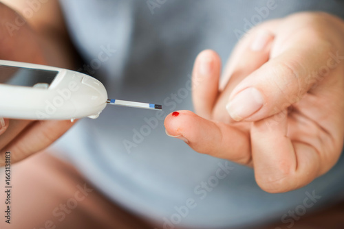 woman with diabetes is using a home blood glucose meter to check her blood sugar level and carefully checks her finger with the meter to control her high blood sugar level.