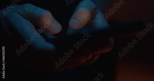 Hands typing at night with phone, texting on the internet in the dark to cyberbullying. Writing comments on social media with a smartphone.