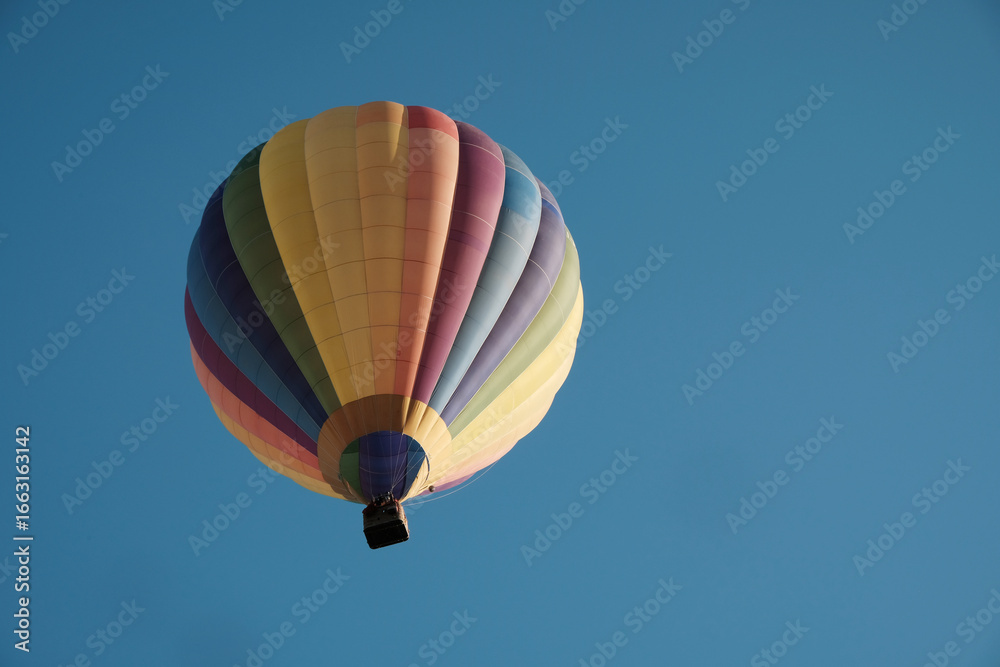 Fototapeta premium Colorful hot air balloon in flight against the sky. Hot air balloons are aircraft that obtain their lift by heating a large envelope of air above ambient temperature. Real photography, not AI.