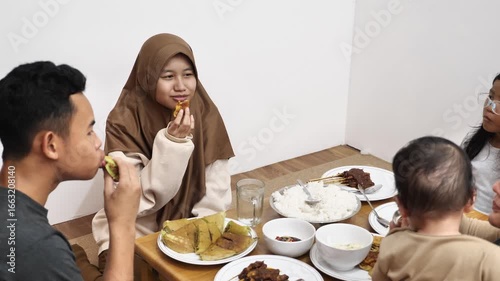Asian muslim family doing chit chat talks while eating dinner, sitting on floor with low dining table