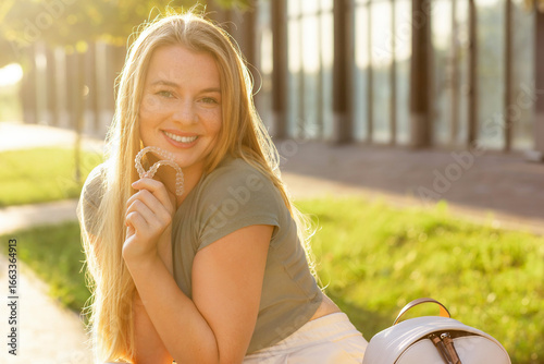 Smiling woman outdoors holding orthodontic aligners for dental correction