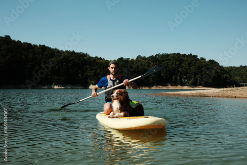 Wallpaper Mural A man with his Australian shepherd dog on a SUP board, paddling on a lake. Outdoor summer activity and pet bonding Torontodigital.ca
