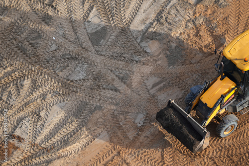 Yellow JCB excavator working at a construction site, top view with detailed tire tracks in the sand
