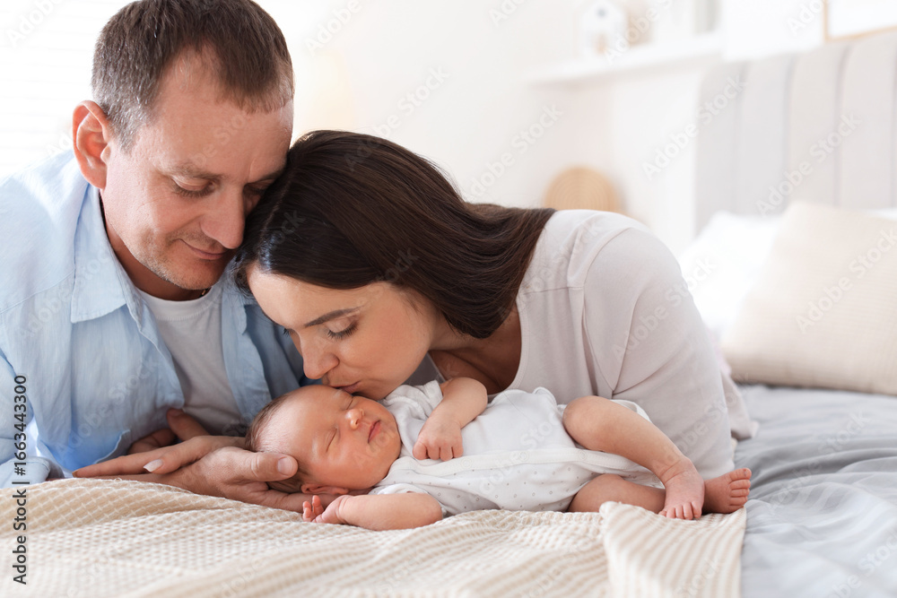 Fototapeta premium Mom and dad with their newborn baby on bed at home