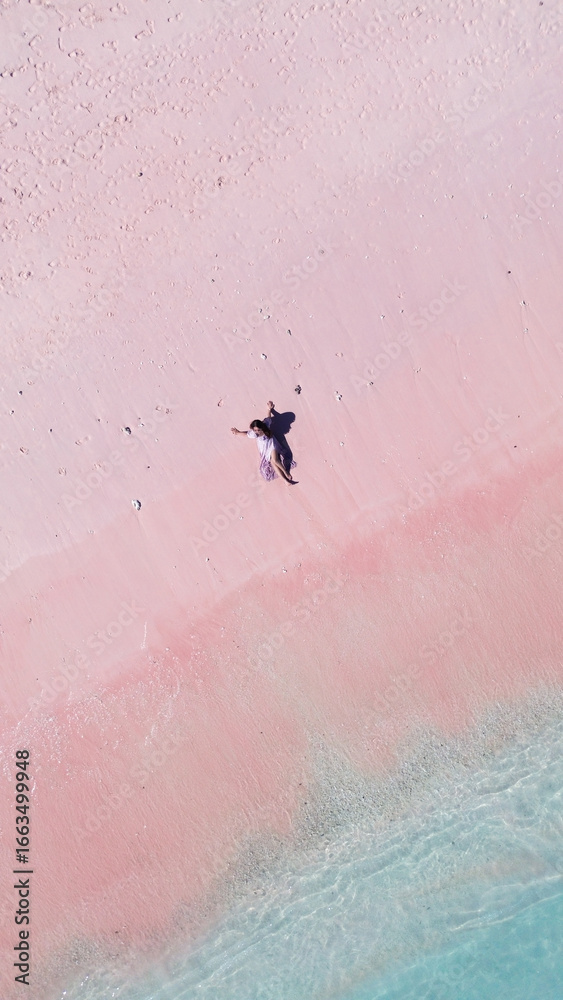 Fototapeta premium Top view of a relaxed young Asian woman laying on the pink sand at Pink Beach, Labuan Bajo.