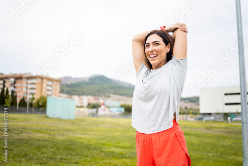 A woman between 40 and 50 years old is training outdoors in sportswear.The woman stretches her arms happily.Concept of middle-aged women doing sports.