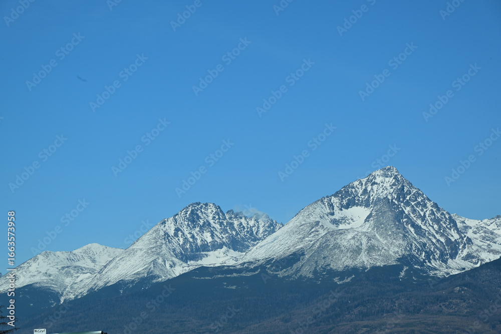 Fototapeta premium A distant view from the hill of the high peaks of snow-capped mountains High Tatra in spring