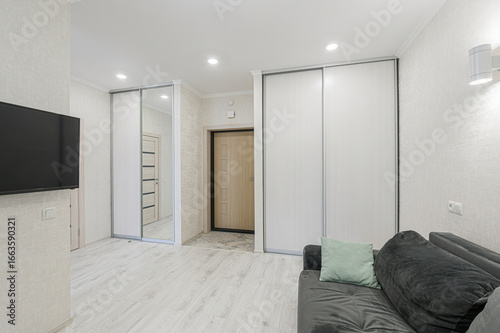 Bright room with a dark sofa, light floors, sliding door wardrobes, and a TV. Interior doors are visible