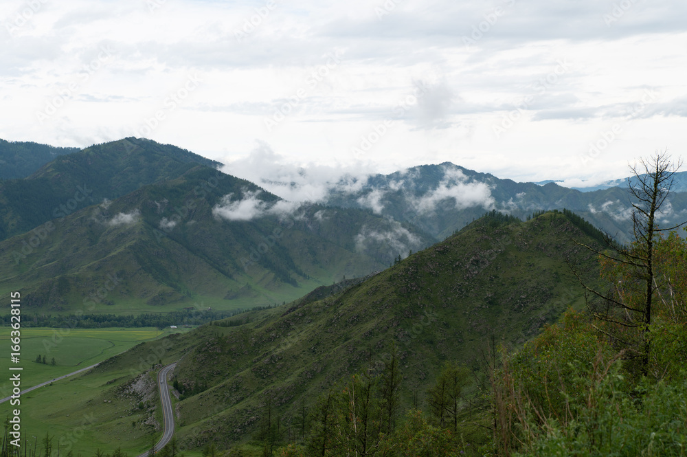 Naklejka premium Mountain valley with lush green grass surrounded by mountain ranges covered with clouds