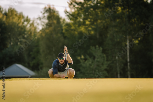 Obraz na plátne Male golfer squats down on the green, lining up his putt with intense focus