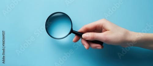 The hand holding a magnifying glass against a blue background.
