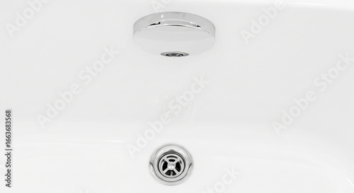 Close-up of a clean white bathtub with modern chrome drain and overflow fixtures