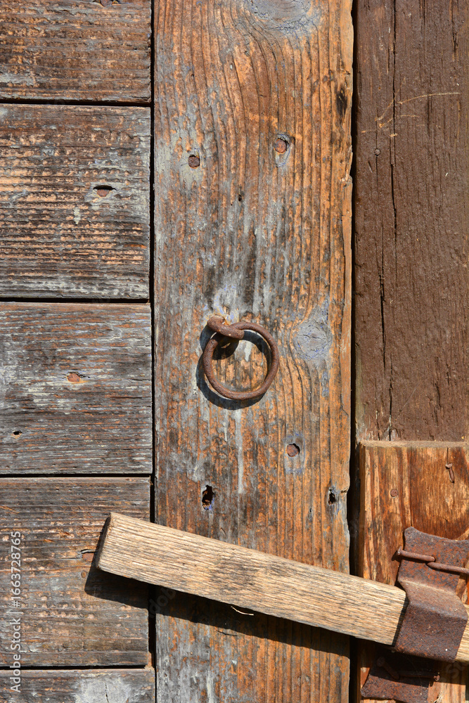 Fototapeta premium A close-up shot of an old wooden door featuring a weathered metal ring and a wooden latch, showcasing texture and patina