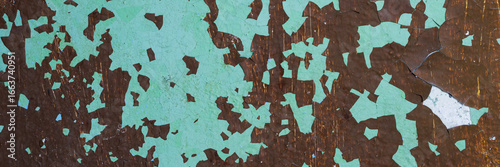 Peeling paint on the wall. Panorama of a concrete wall with old cracked flaking paint. Weathered rough painted surface with patterns of cracks and peeling. Wide panoramic texture for design background
