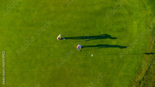 Fotografie Golfers playing on green grass golf course on sunny day, aerial view