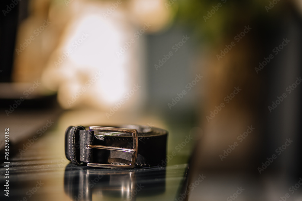 A stylish black leather belt with a silver buckle rolled up neatly on a reflective surface, captured with warm background bokeh and soft lighting. A stylish black leather belt with a silver buckle rolled up neatly on a reflective surface, captured with warm background bokeh and soft lighting.