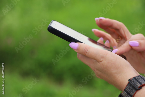 Smartphone in female hands, woman using mobile phone outdoor at summer