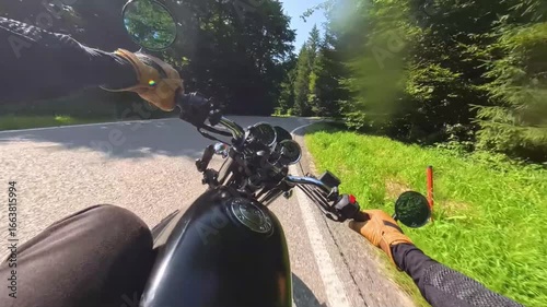 Riding motorcycle through the green forest on a sunny summer day on a curvy road