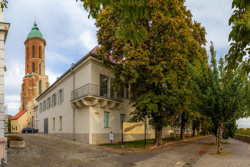 Obraz premium Peaceful Arpad Toth Promenade with yellow-green autumn trees, featuring Mary Magdalene Bell Tower against blue sky in Buda Old Town. Budapest, Hungary.