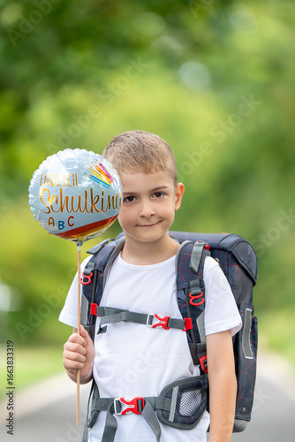 Fröhlicher Erstklässler mit Schulranzen und Ballon „Schulkind“ – Porträt eines Jungen am ersten Schultag, Einschulung, Schulanfang, Grundschule, Bildung, deutsche Tradition