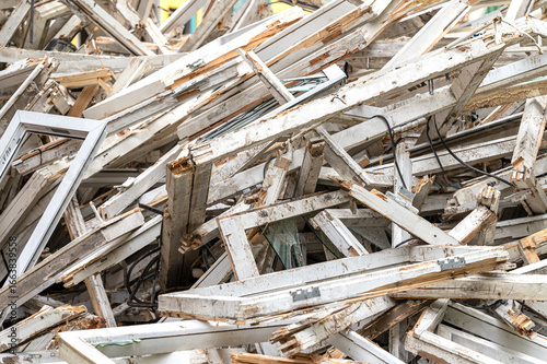 A large pile of broken, weathered white wooden window frames and debris.  Some pieces show remnants of glass and metal hinges