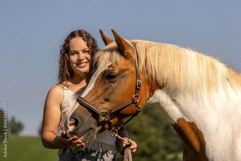 Obraz premium Young woman bonding with Haflinger crossbreed pinto mare outdoors in summer