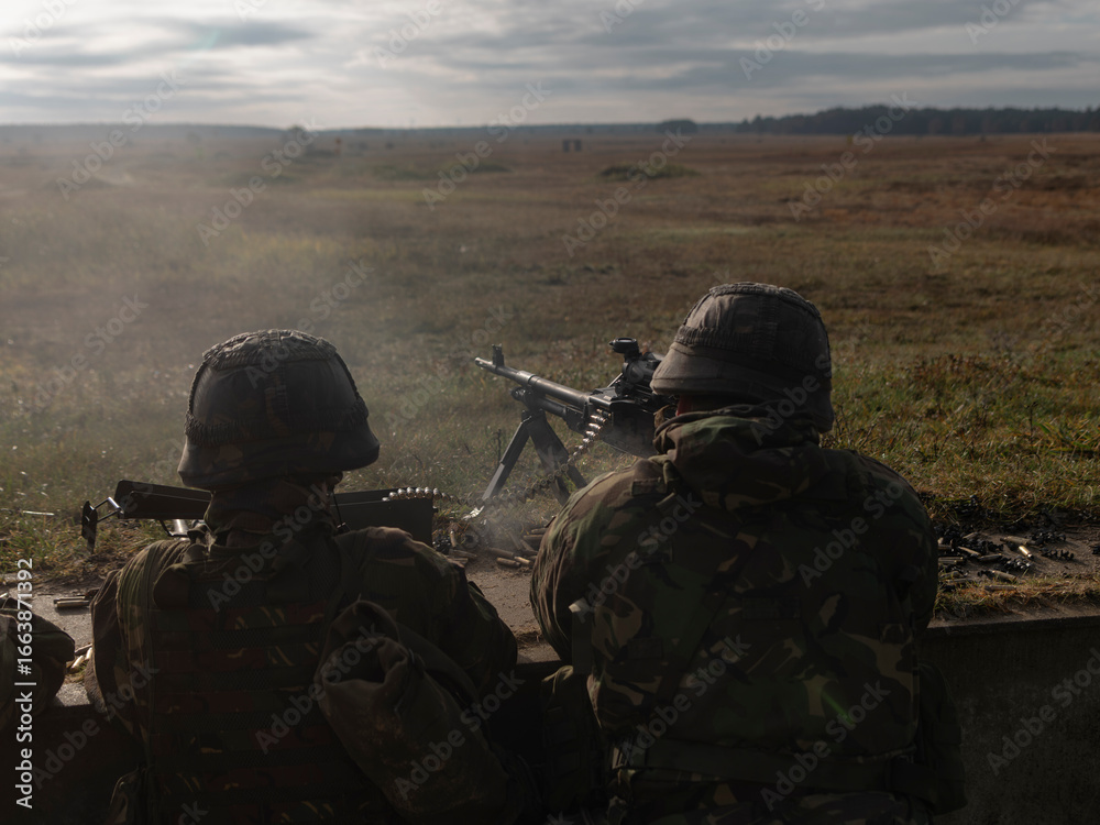 Fototapeta premium Military personnel operating machine gun from field position overlooking training area
