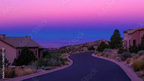 A winding road through a hillside neighborhood at twilight, with a vibrant purple and pink sunset.