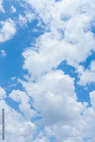 Bright blue sky with fluffy white cumulus clouds A vertical image showing a mostly sunny day