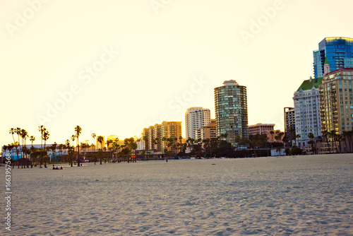 Golden hour over Long Beach, California, with palm trees lining the sandy beach and modern high-rise buildings glowing against the Pacific coastal skyline.