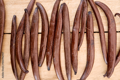 Vanilla pods displaying rich brown hue, lying on weathered wooden surface, highlighting natural texture and culinary potential