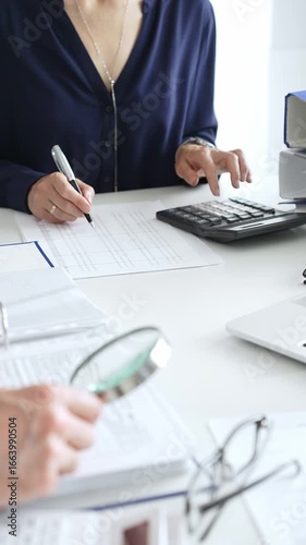 Female financial analysts with male colleague examining documents, using magnifying glass and calculator while examining corporate data at workplace in office. Audit and taxes in business