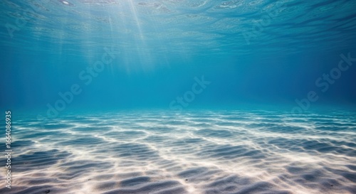 Sunlight streams through the clear blue ocean water, illuminating the sandy seabed below with beautiful patterns