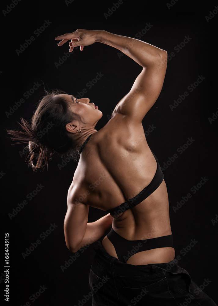 Obraz premium Strong athletic woman in black sportswear showing muscular body and six pack abs while dancing gracefully on black background. 