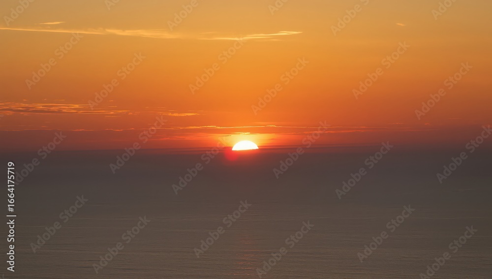 Obraz premium A bright sun setting over a hazy horizon with orange and yellow sky and dark water below it all