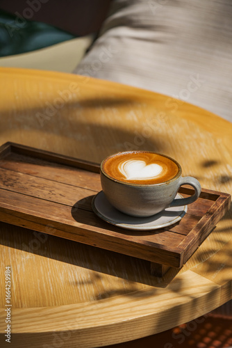 latte coffee art on wooden plate at desk in sun shine with shade of the tree