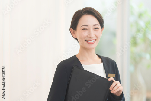 Obraz na płótnie コンシェルジュ。ジャケットを着て黒いファイルを持つ笑顔の日本人女性。