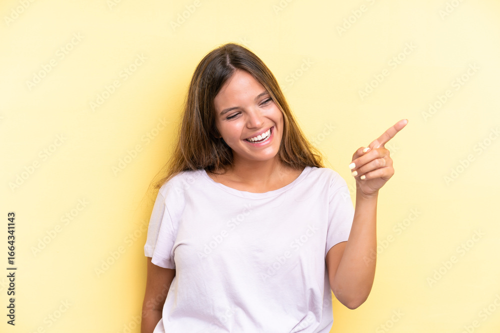 Young caucasian woman isolated on yellow background pointing finger to the side and presenting a product Young caucasian woman isolated on yellow background pointing finger to the side and presenting a product